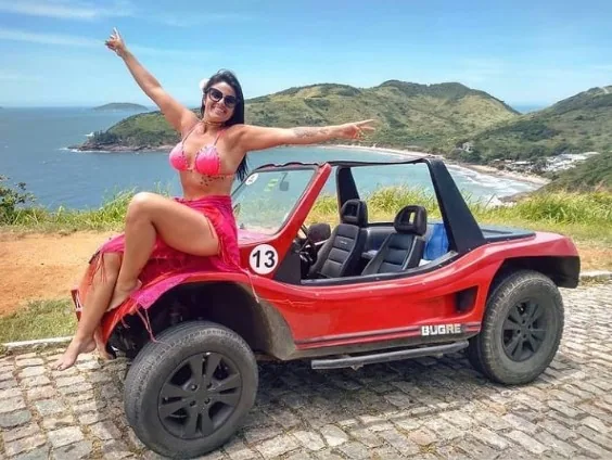 Turista sentada sobre buggy vermelho em mirante com paisagem costeira de Búzios